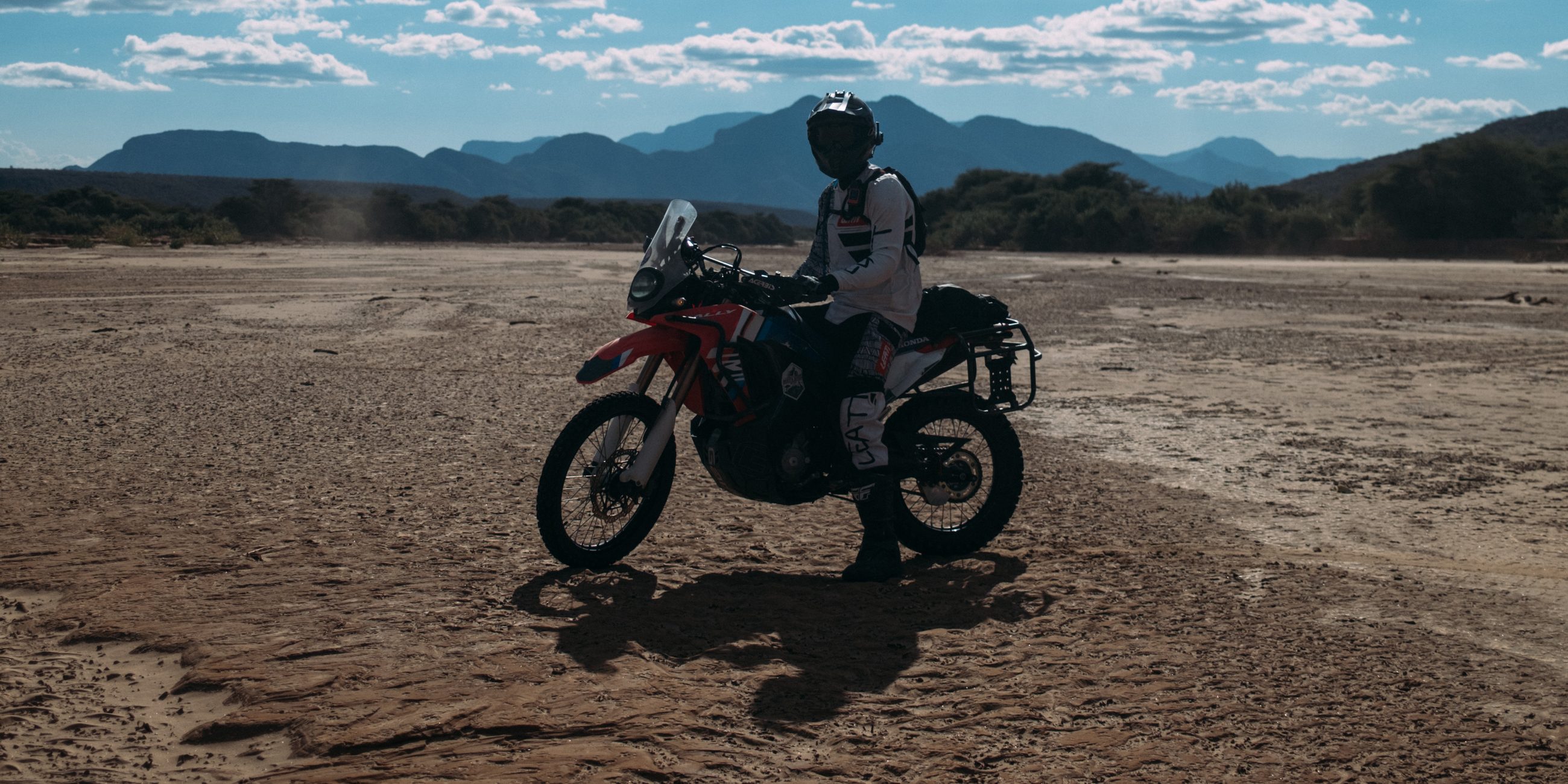 A rider on a dry riverbed with mountains behind