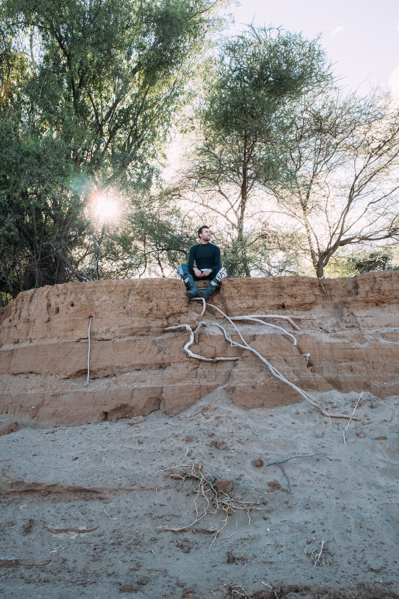 A tent and a bedroll set out on a dry riverbed beneath acacias