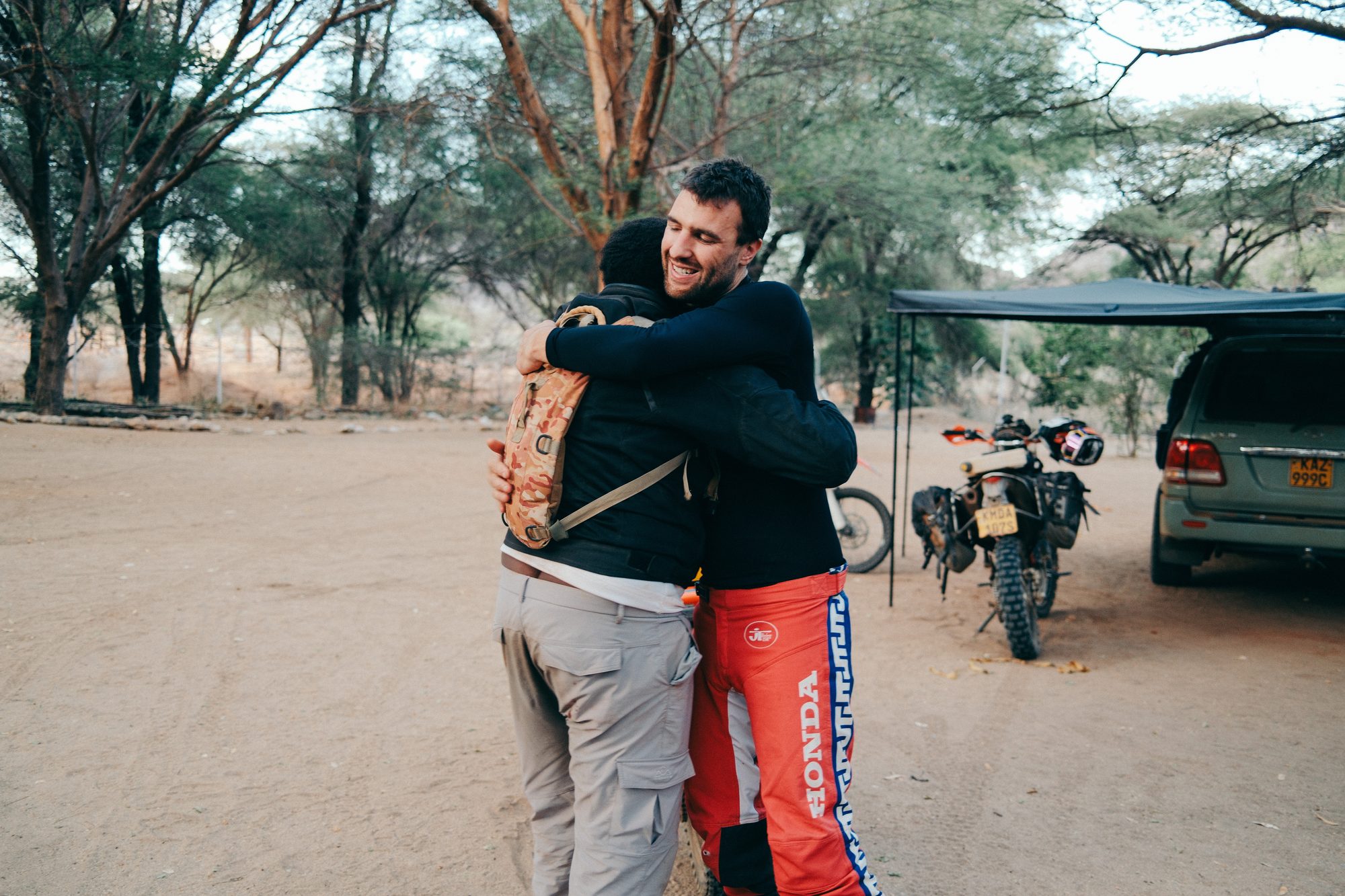 Two riders embracing beside the bikes under acacia trees