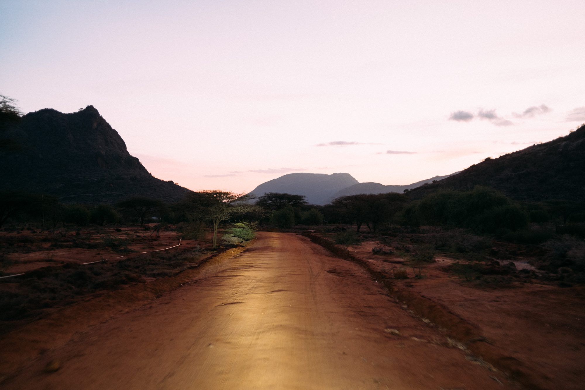 A red-earth road running towards mountains at dusk in northern Kenya