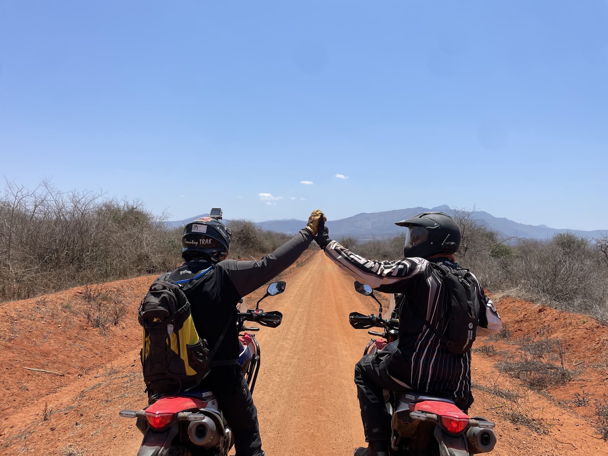 Two riders reaching across to each other on a red dirt road